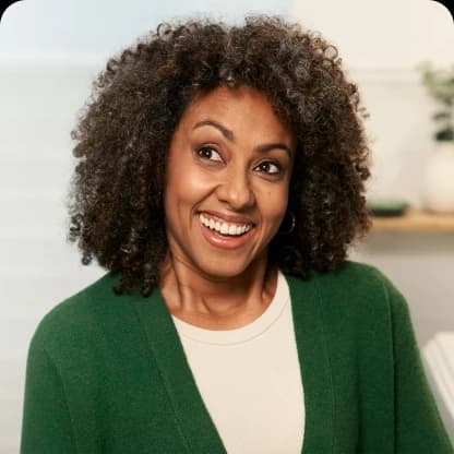 Smiling woman with curly hair wearing a green sweater and earrings.