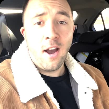 Person in a car wearing a brown jacket with a white fleece collar.