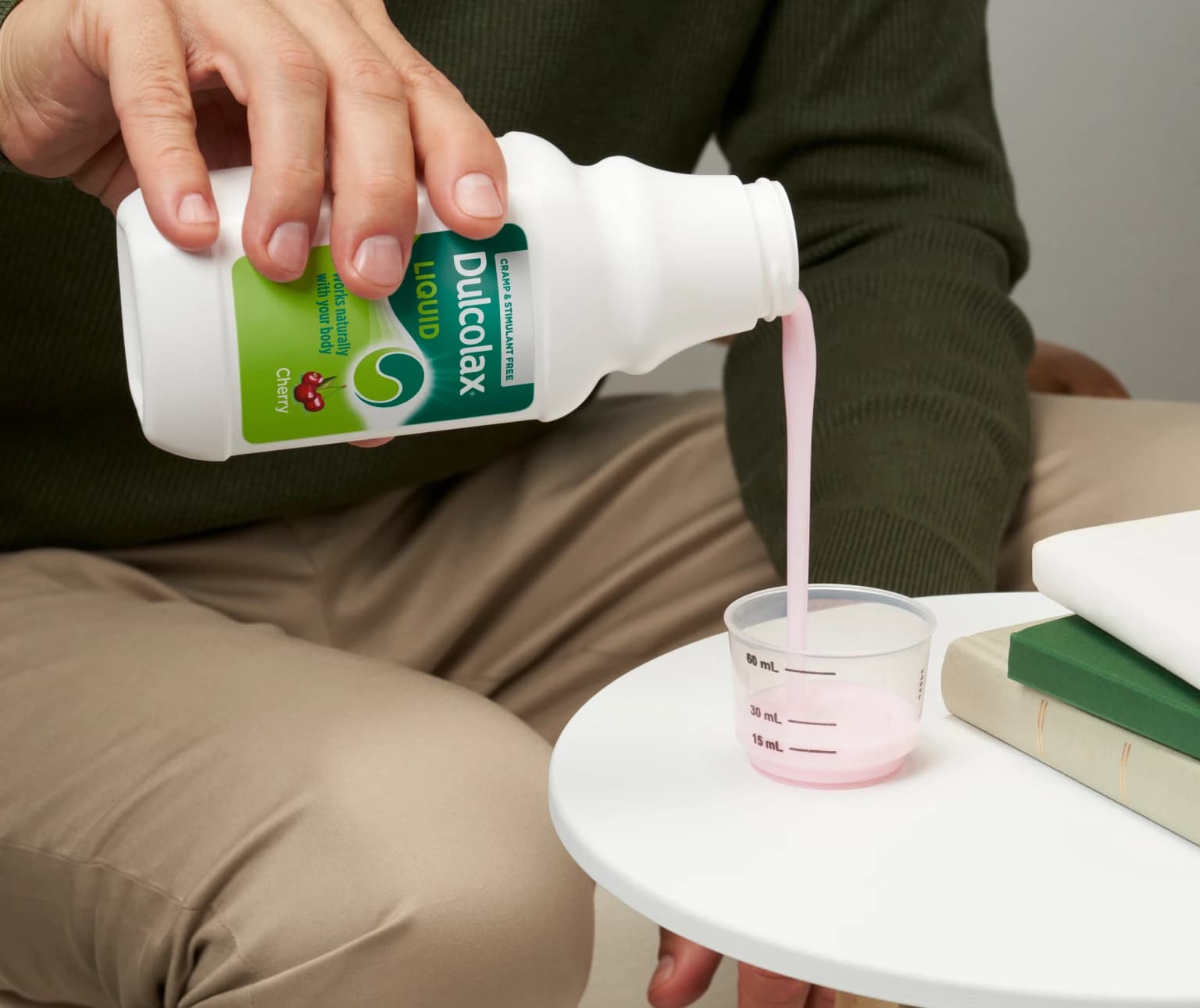 Person pouring pink Dulcolax Liquid Cherry into a measuring cup on a table.